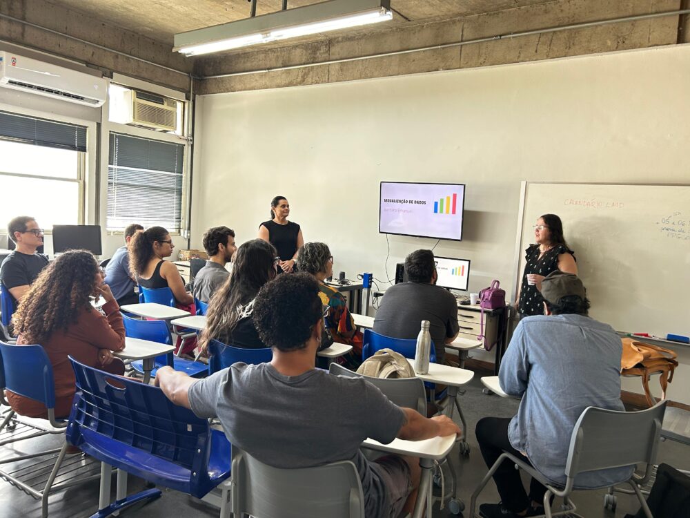 Professora doutora Bárbara Emanuel, da UFF, ao lado da professora doutora Raquel Lobão, apresentando slides para vários alunos sentados em uma sala.