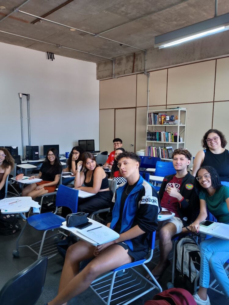 Foto dos participantes da oficina sentados e a professora Mayara Barros de pé entre os alunos.